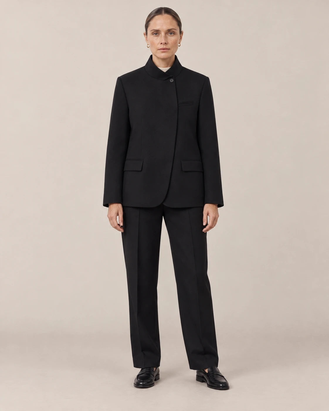 Mujer con blazer negro de cuello mao y pantalón negro de frente en un estudio