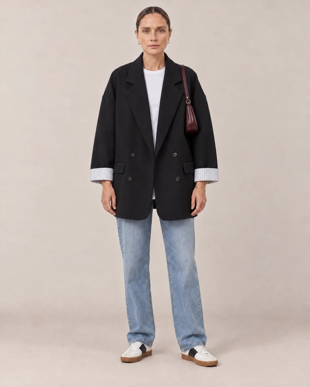 Mujer con blazer cruzado oversize negro, camiseta blanca y vaqueros en un estudio