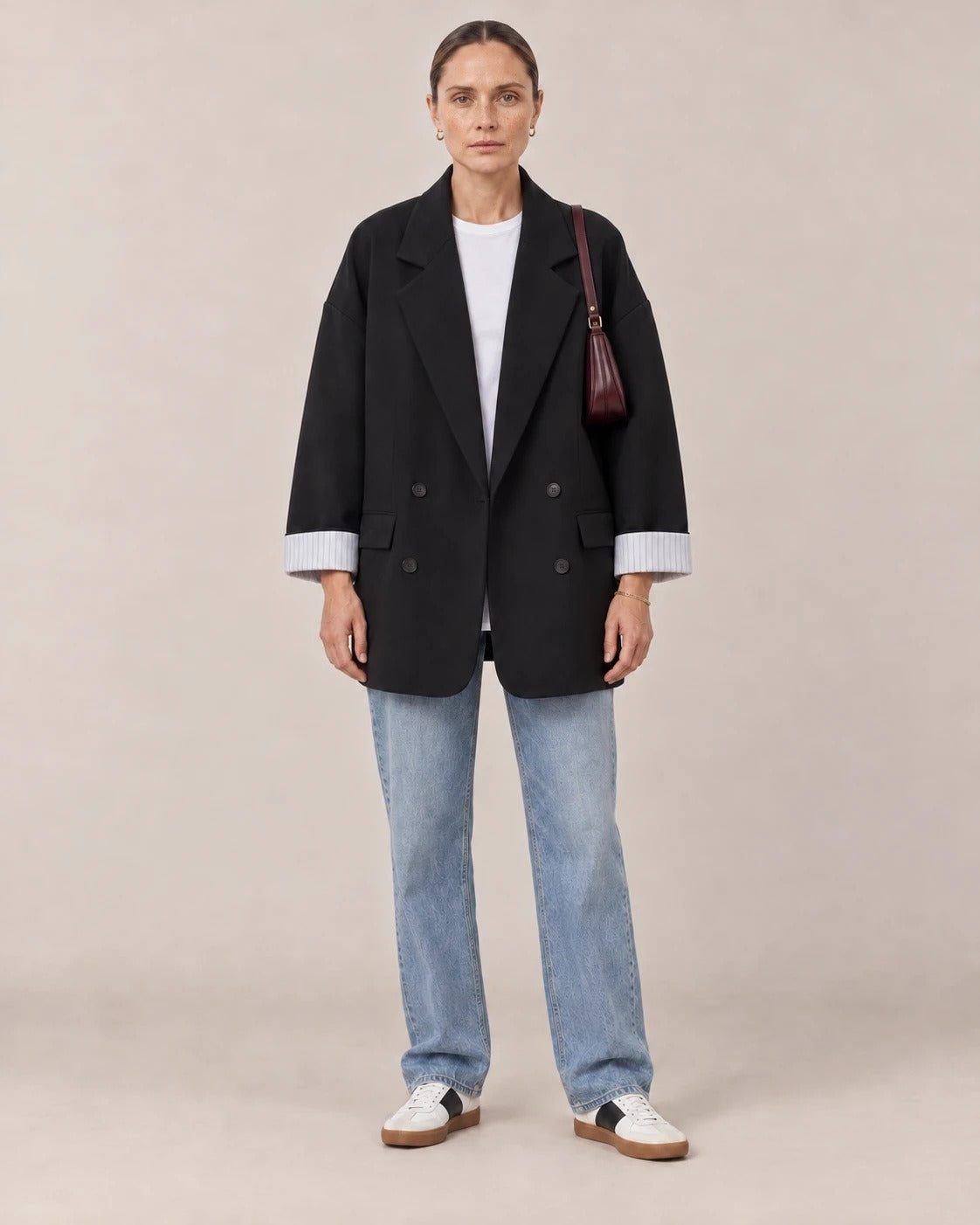 Mujer con blazer cruzado oversize negro, camiseta blanca y vaqueros en un estudio