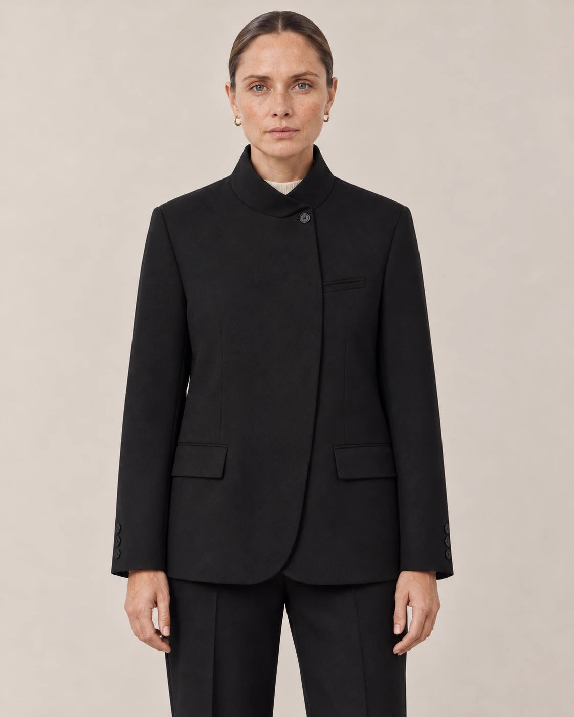 Detalle del cuello mao, el botón y los bolsillos con solapa del blazer negro