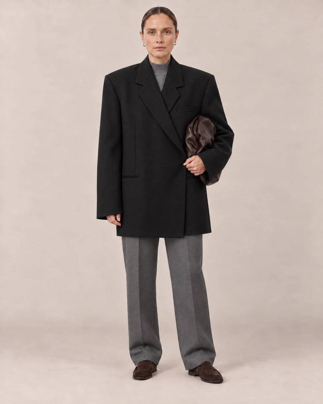 Mujer con blazer oversize negro sobre conjunto gris en un estudio
