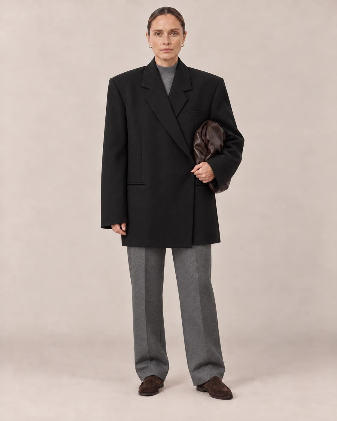 Mujer con blazer oversize negro sobre conjunto gris en un estudio