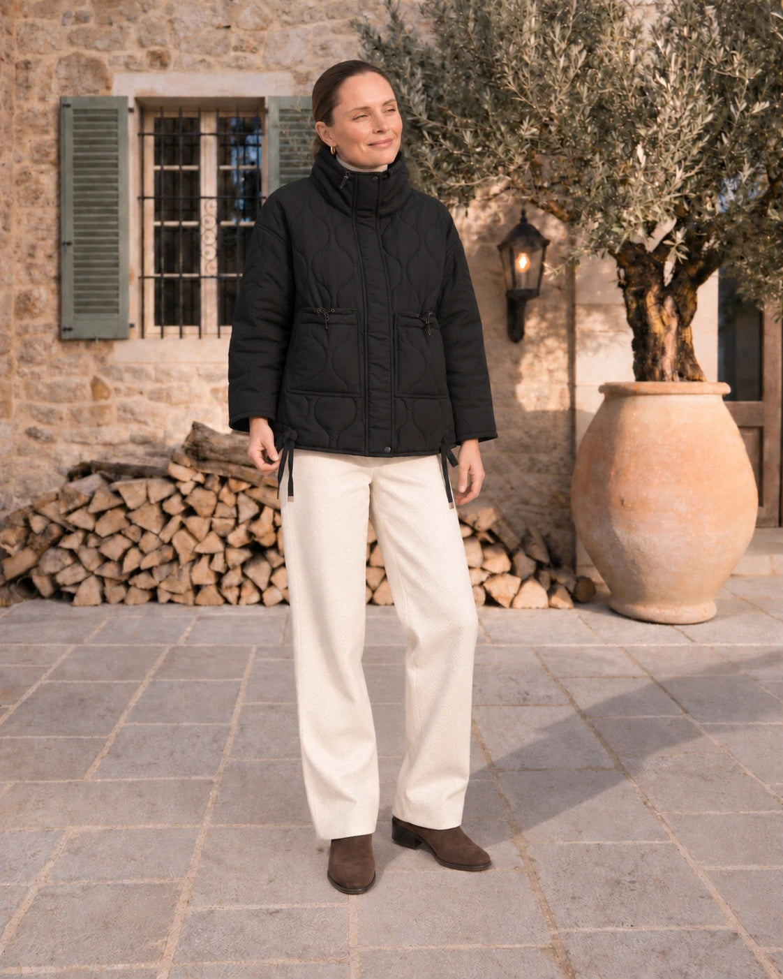 Mujer con chaquetón acolchado negro al sol de invierno junto a un olivo