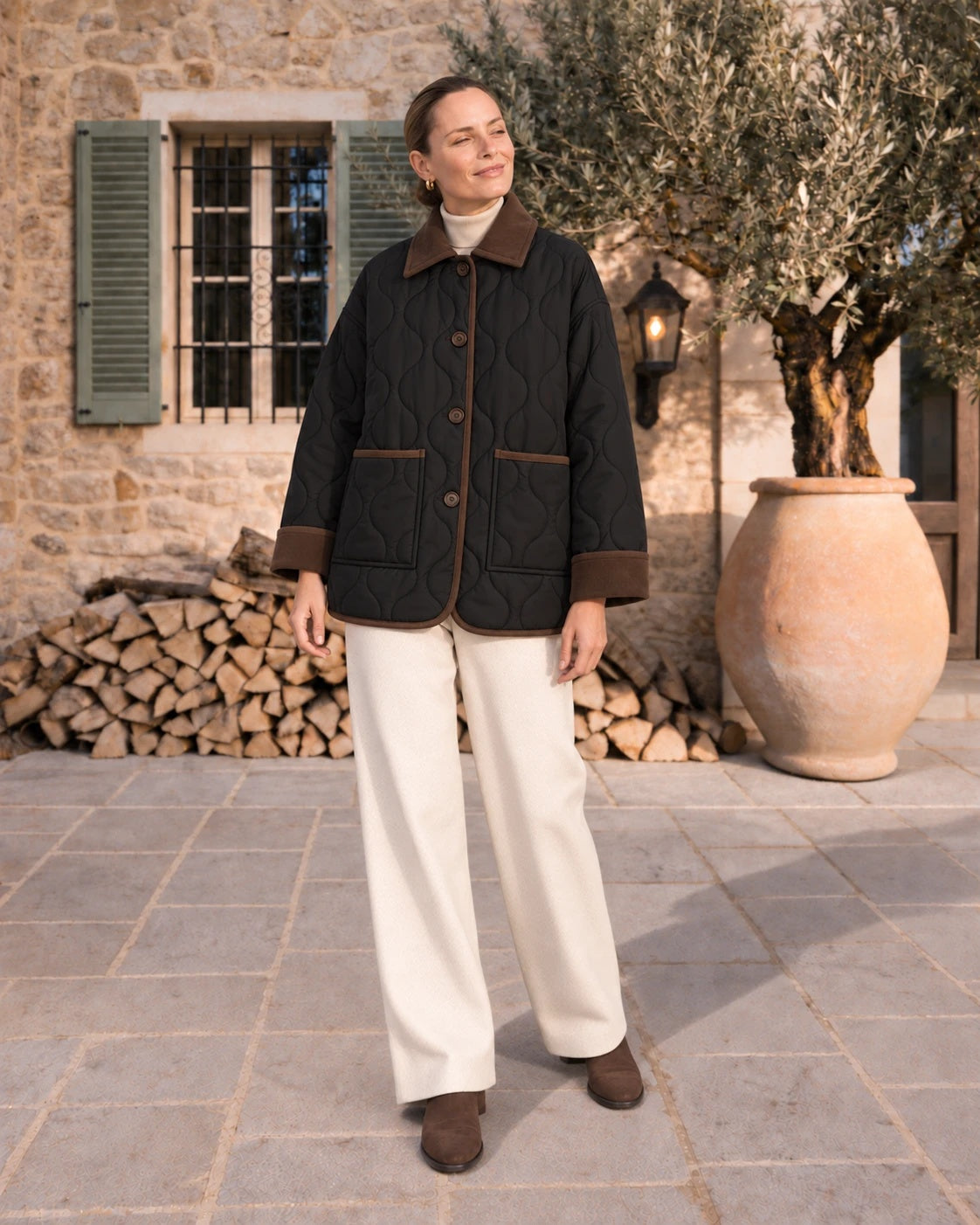Mujer con chaquetón acolchado negro al sol de invierno junto a un olivo